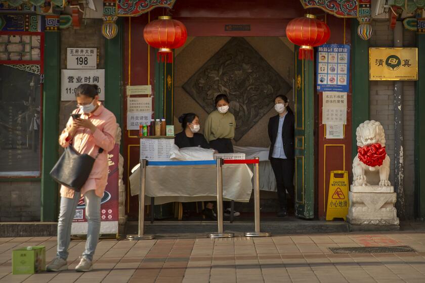 Clerks wear face masks to prevent the spread of the new coronavirus as they wait for customers at the entrance to a restaurant in Beijing, Tuesday, April 28, 2020. The Chinese city of Wuhan, which was the original epicenter of the pandemic, again reported no new coronavirus cases or deaths Tuesday and its hospitals remained empty of virus patients for a second straight day. (AP Photo/Mark Schiefelbein)