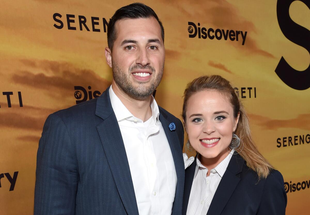 Jeremy Vuolo and Jinger Duggar Vuolo smile and pose together in dark blue suits.