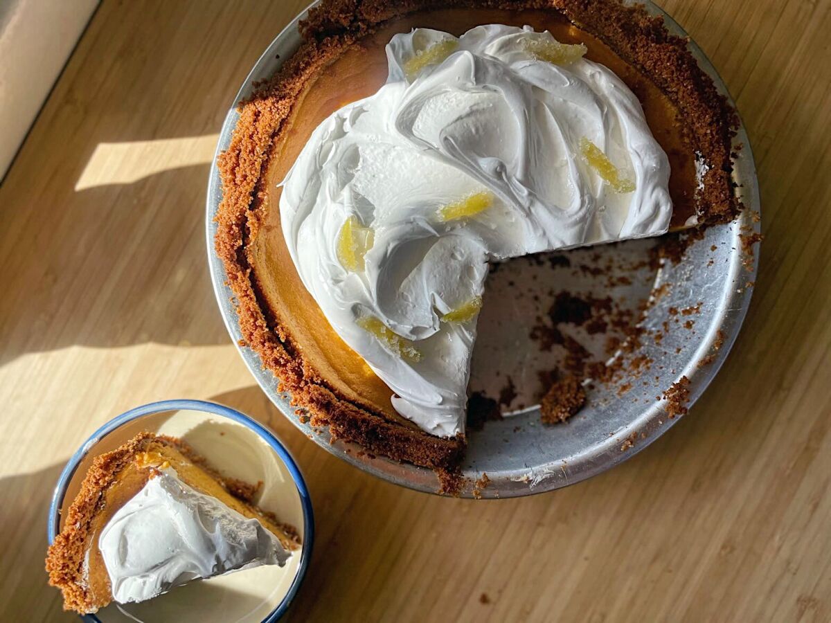 An overhead photo of Sasha Piligian's ginger-and-pumpkin pie on a wooden counter. A slice has been removed and plated.