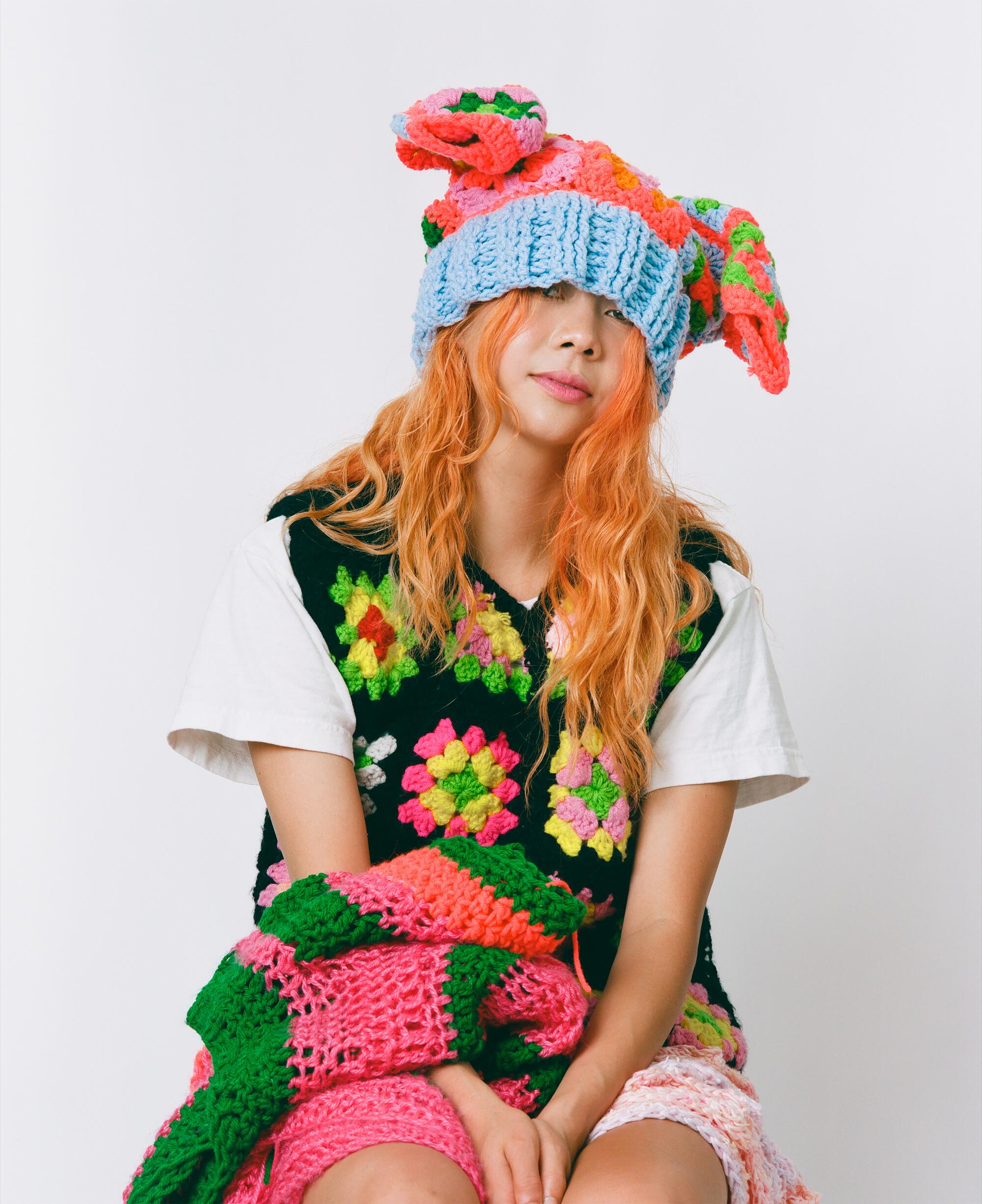A woman with orange hair wears a fully crocheted colorful outfit.