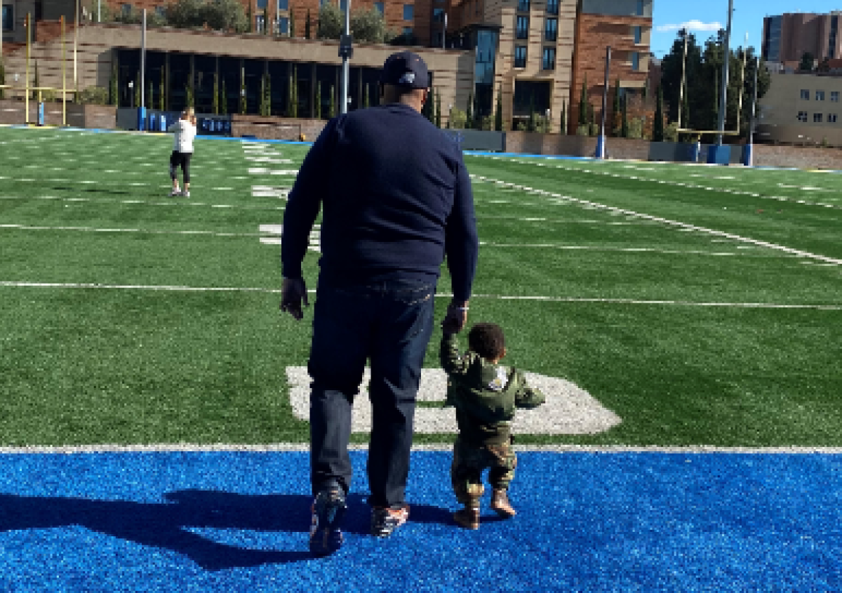 Former Cal State Fullerton football player Dennis S. Ellis walks on a football field with his young son, Townsend.