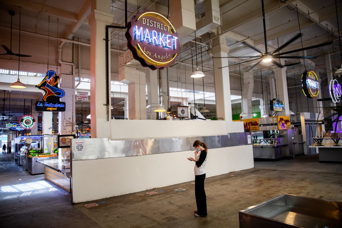 A woman checks her phone in a quiet area of a mostly empty Grand Central Market in downtown Los Angeles