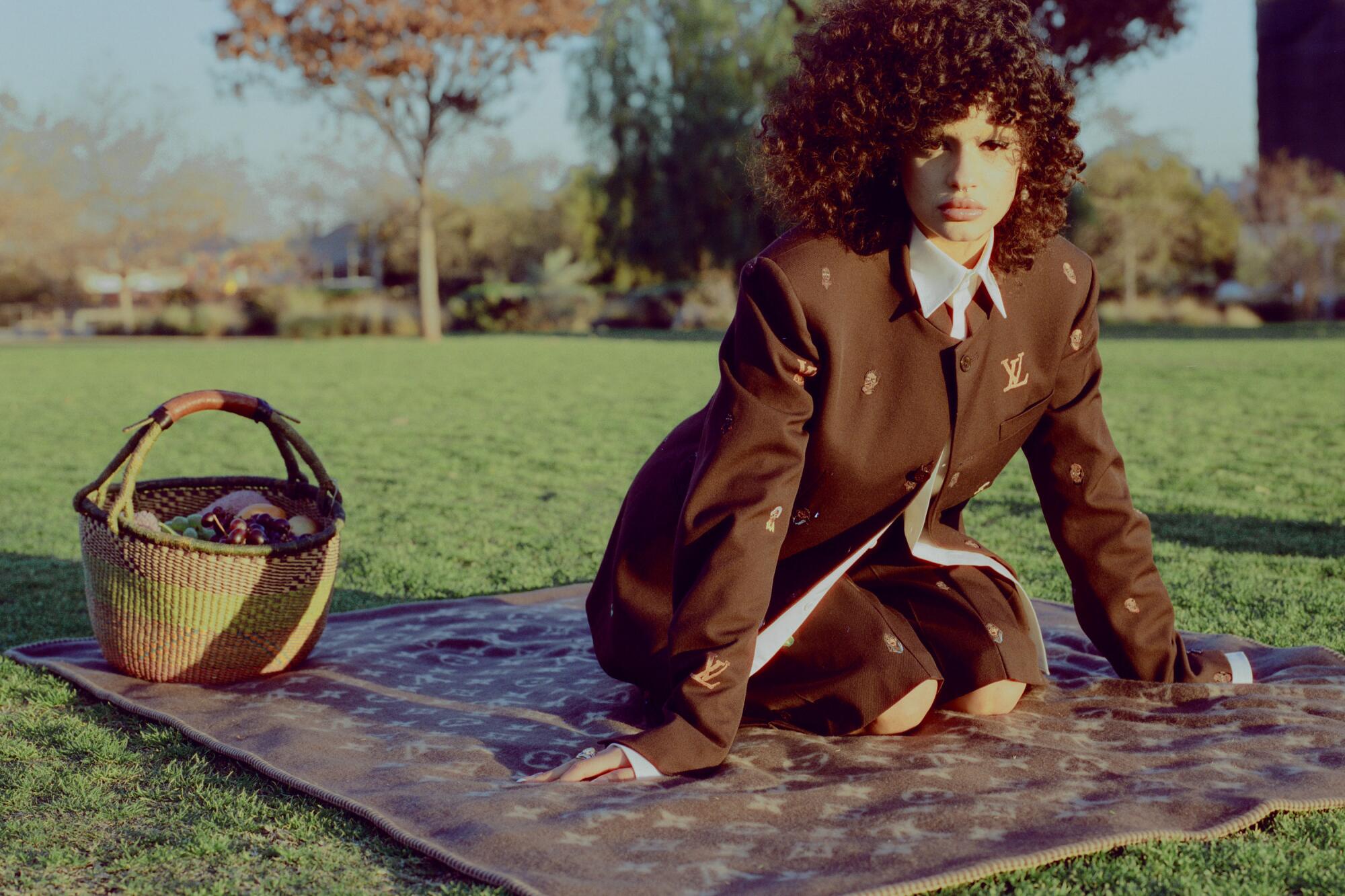 Model wears Louis Vuitton outfit on a picnic blanket in the park.