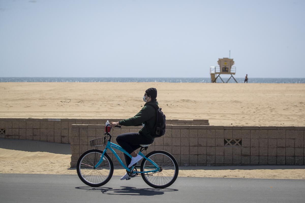 A man wears a protective mask while biking on the mostly empty boardwalk in Huntington Beach on Thursday.