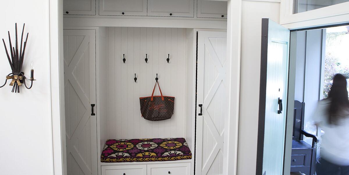 A mudroom off the entryway has cushioned seating, twin wardrobes for coats and wall hooks to hang hats and purses.