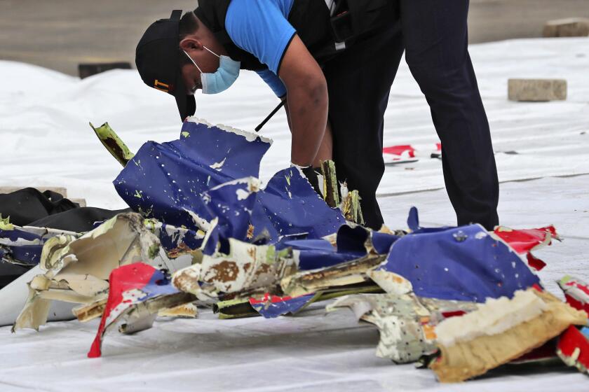 An investigator of Indonesian National Transportation Safety Committee inspects parts of Sriwijaya Air Flight 182 that crashed in the waters off Java Island, at Tanjung Priok Port in Jakarta, Indonesia, Sunday, Jan. 10, 2021. Indonesian rescuers pulled out body parts, pieces of clothing and scraps of metal from the Java Sea early Sunday morning, a day after the Boeing 737-500 with dozens of people onboard crashed shortly after takeoff from Jakarta, officials said. (AP Photo/Tatan Syuflana)