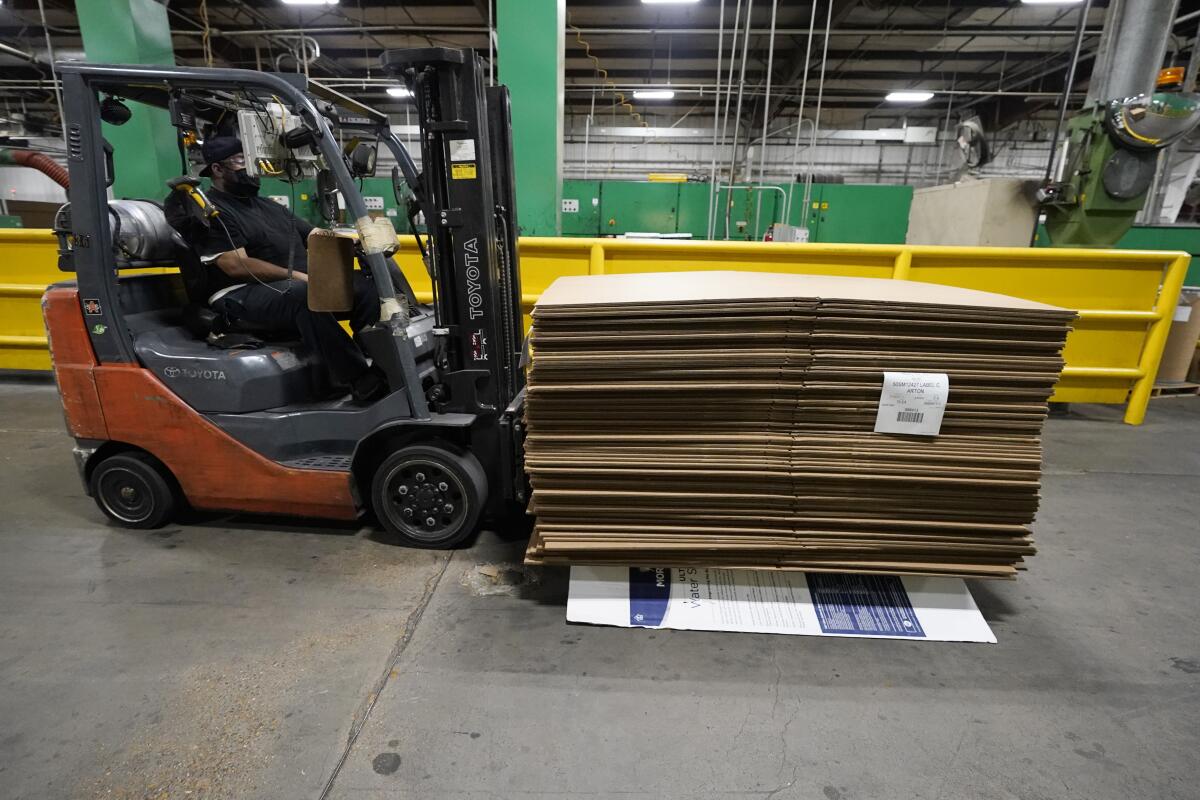 A forklift driver moves a pallet of cardboard boxes.