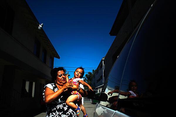 Catherine Carrasco, 53, lives with her two daughters and one son in a two-bedroom apartment in an area of Santa Ana that has a high concentration of single-parent families. Though she works, she has barely been able to afford the rent since the passing of her husband in 2010. Here she holds a next-door neighbor's child, 17-month-old Fatima Leon. See full story