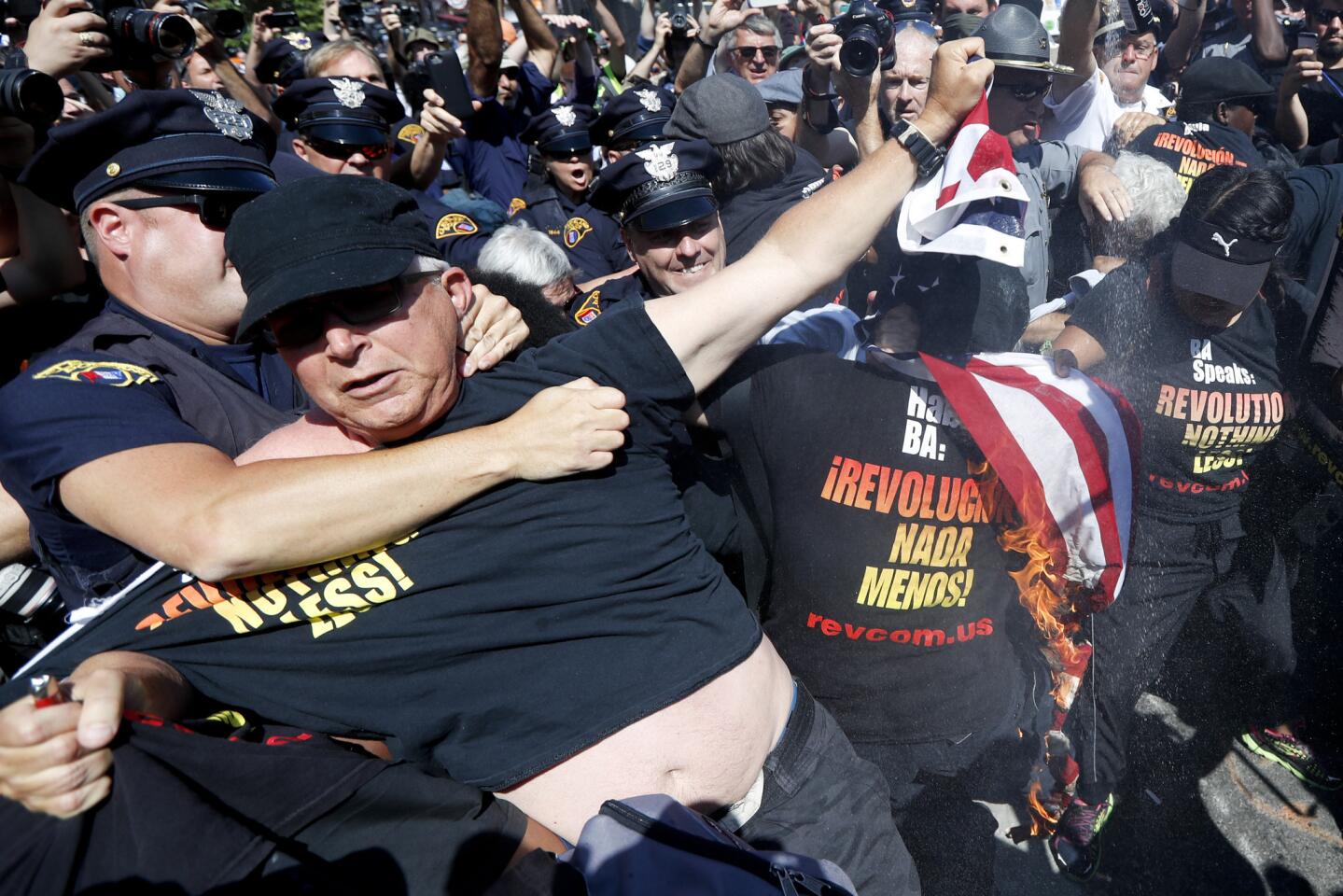 A law enforcement officer clashes with a protester holding a burning American flag, Wednesday, July 20, 2016, in Cleveland, during the third day of the Republican convention.