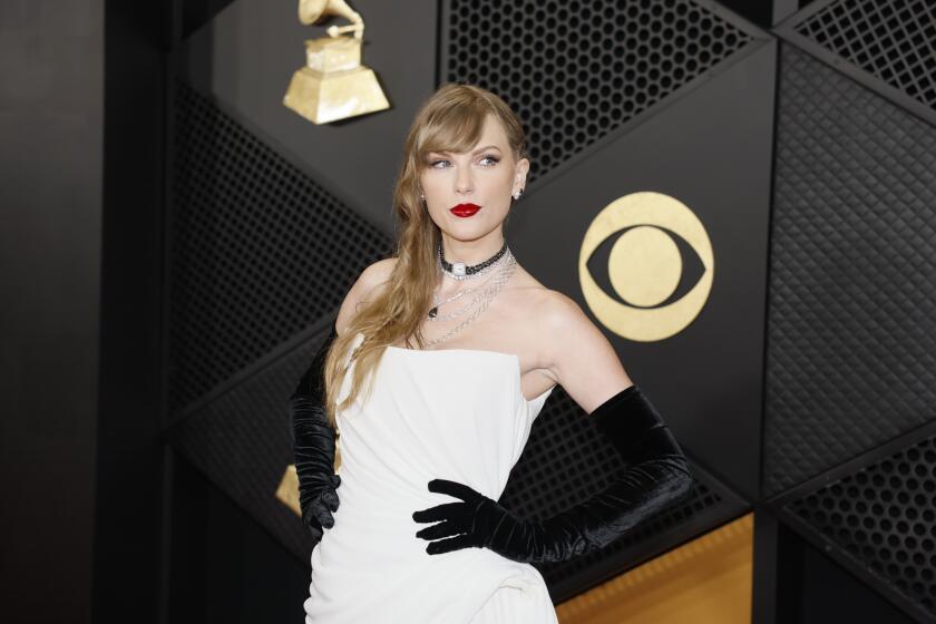 Taylor Swift in a white strapless dress and black gloves posing with her left hand on her hip against a black background