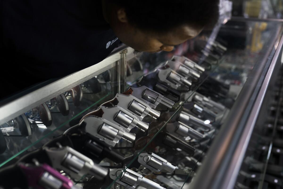 Man leans over a display case with rows of handguns