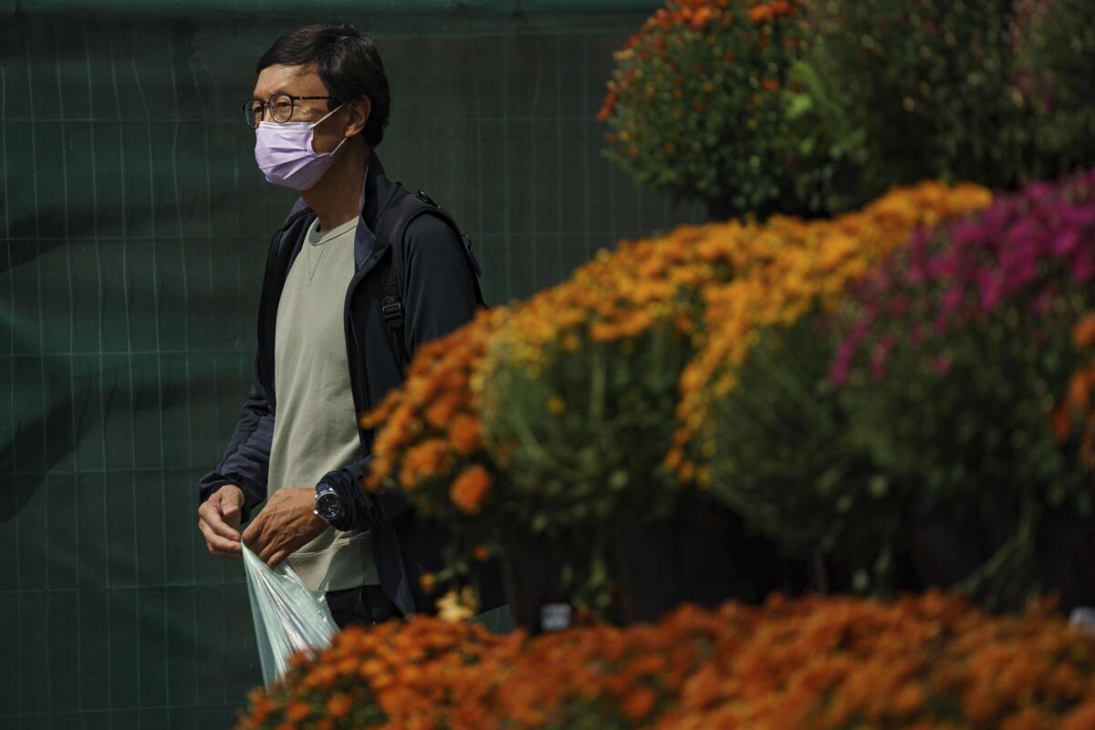 A person wears a mask while walking past a flower display 
