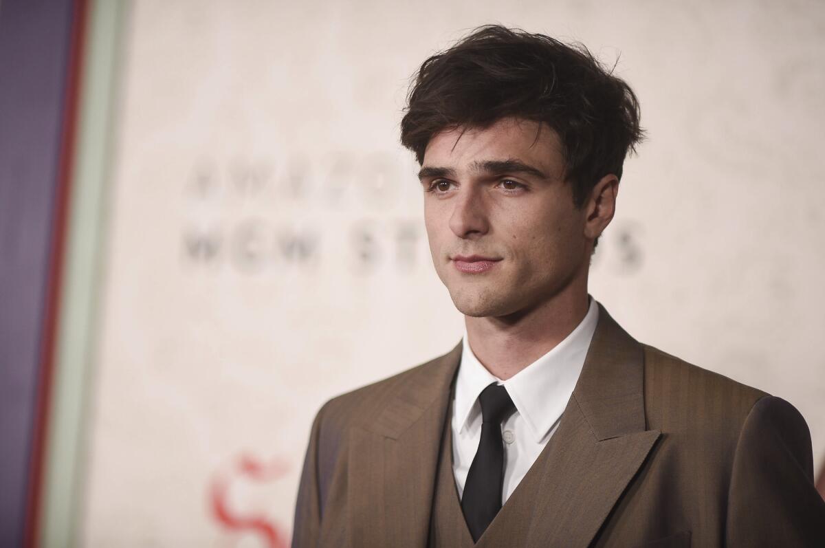 Jacob Elordi, a young man with short, dark brown hair in a brown suit and tie, poses against a beige background