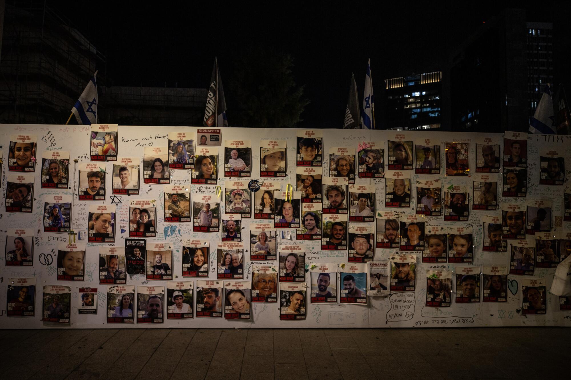 An exterior wall at night, covered in photos of individuals