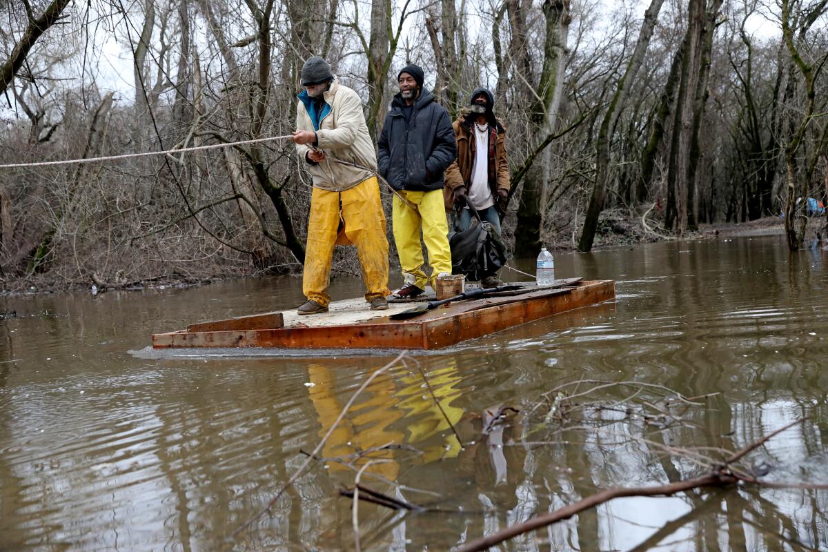 Dyrone Woods, center, who is homeless, takes a raft to check on temporary shelter in Sacramento.