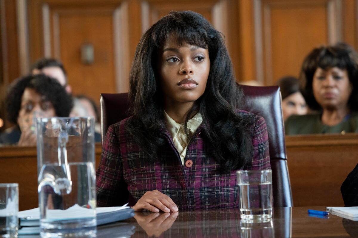 A woman in a purple plaid suit sitting in a courtroom