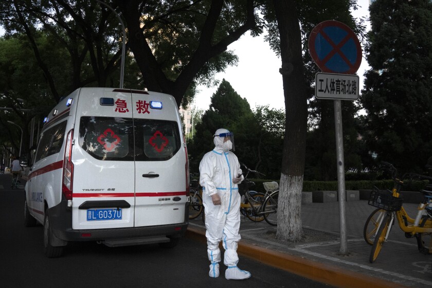 Un trabajador con traje protector contra el coronavirus espera junto a una ambulancia 