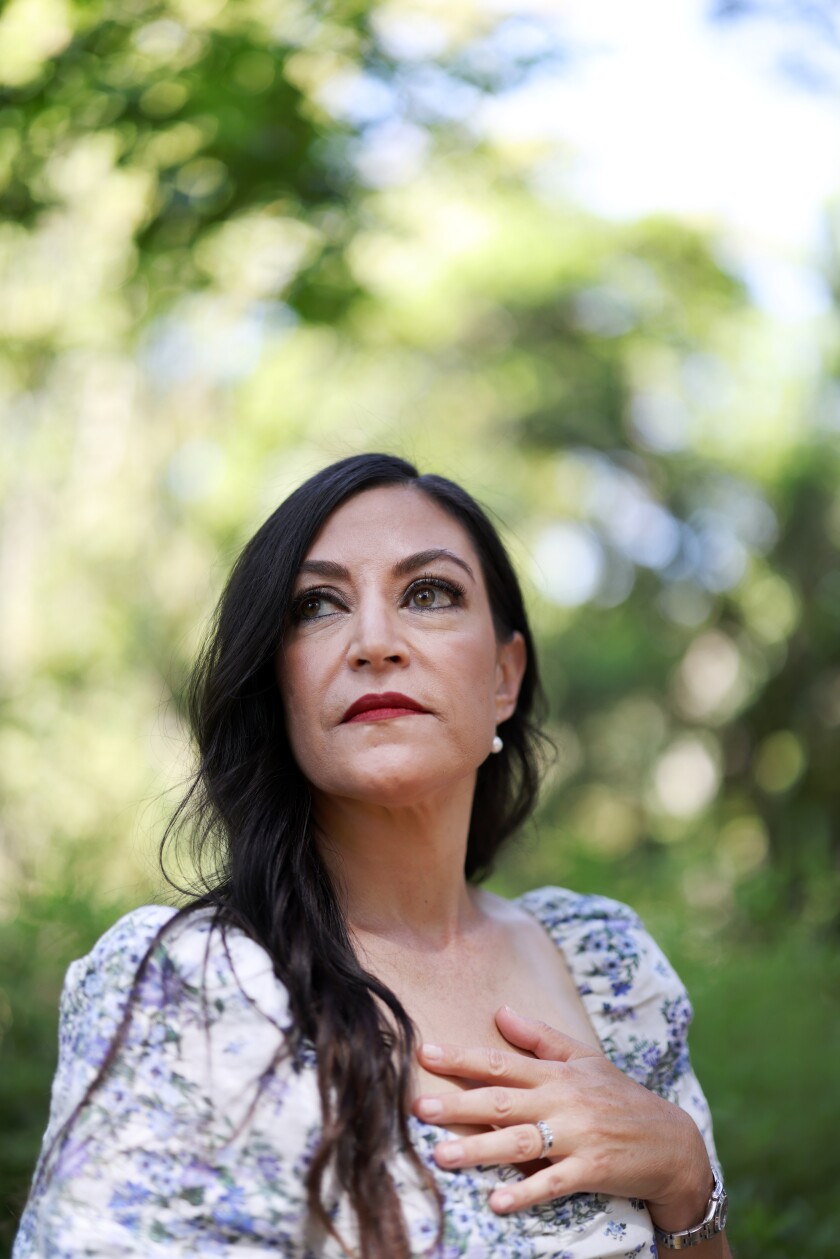 A woman poses outdoors with her hand on her chest