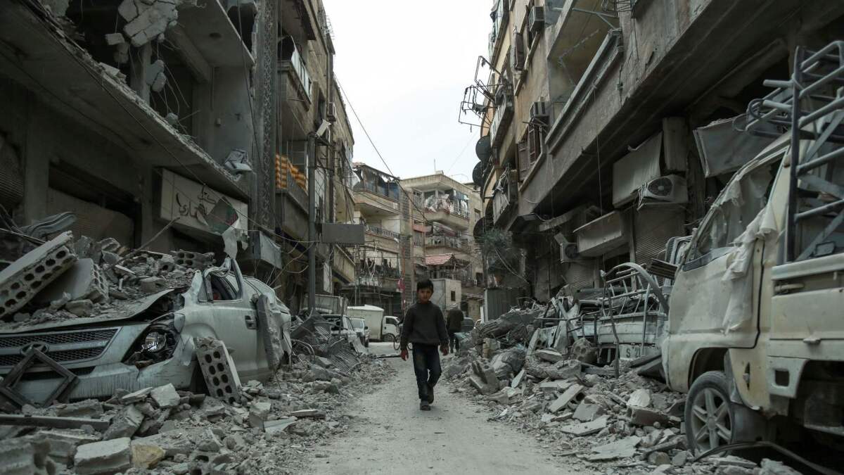 A Syrian child walking down a street past rubble from destroyed buildings, in the rebel-held town of Douma