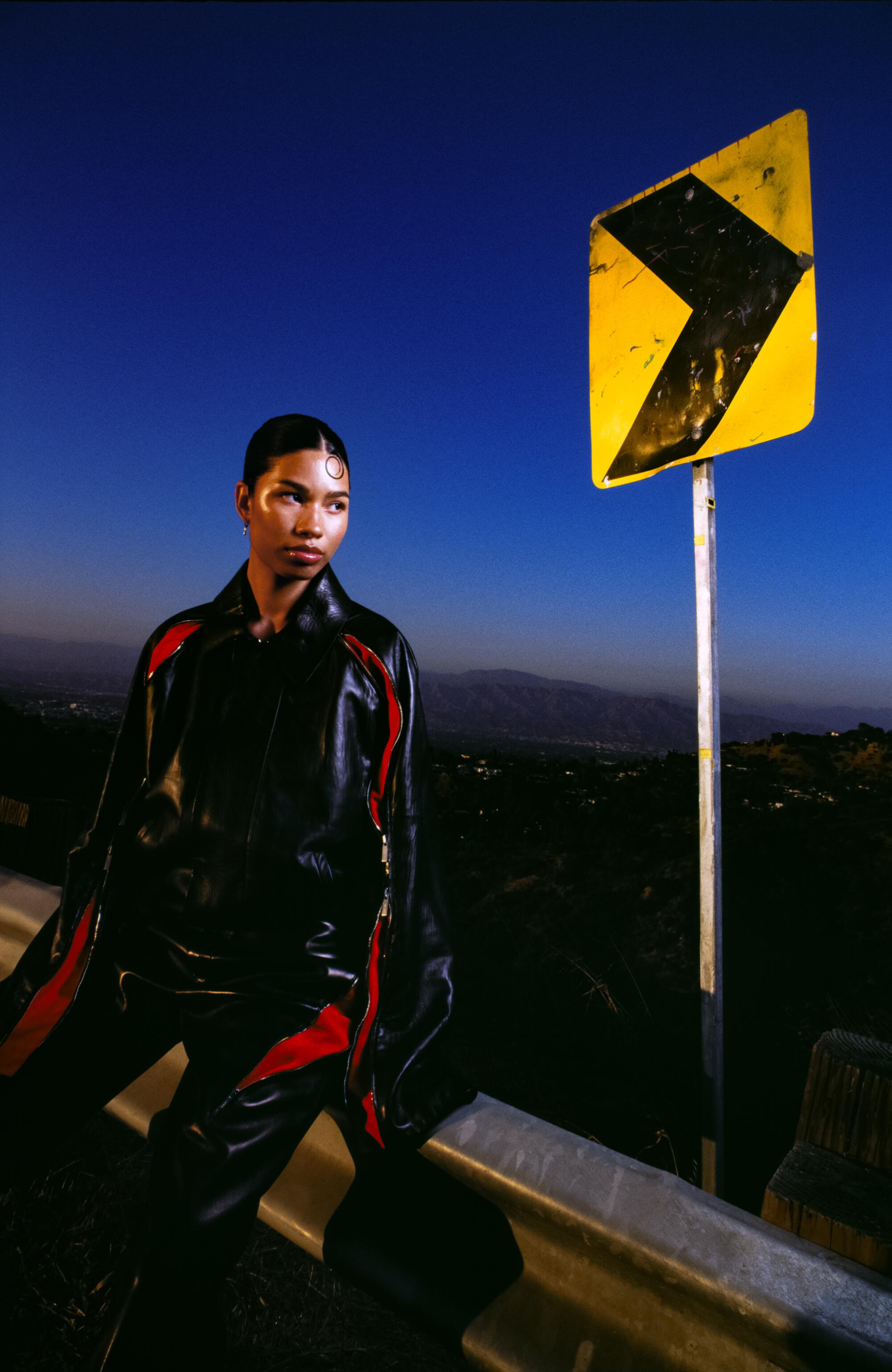 A model wears Ferragamo leather jacket and pants and stands next to a yellow road sign.