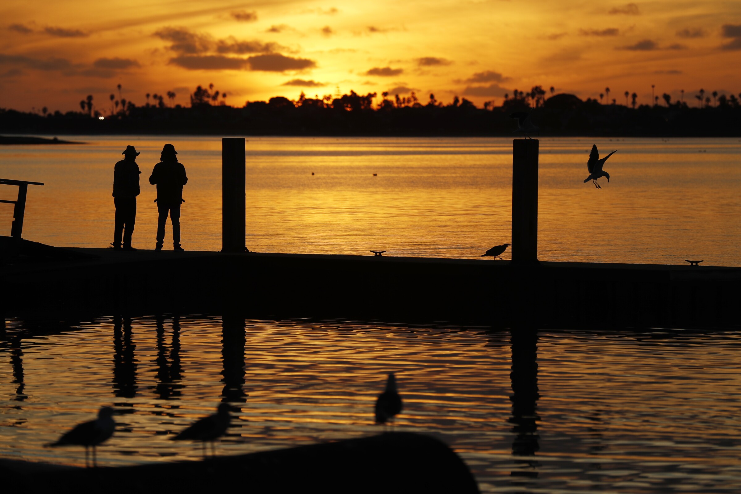 People watch the sunset from a dock on Mission Bay on a chilly night in San Diego on Sunday, Dec. 26, 2021.
