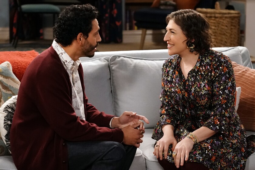 Christopher Rivas and Mayim Bialik face each other on a couch.