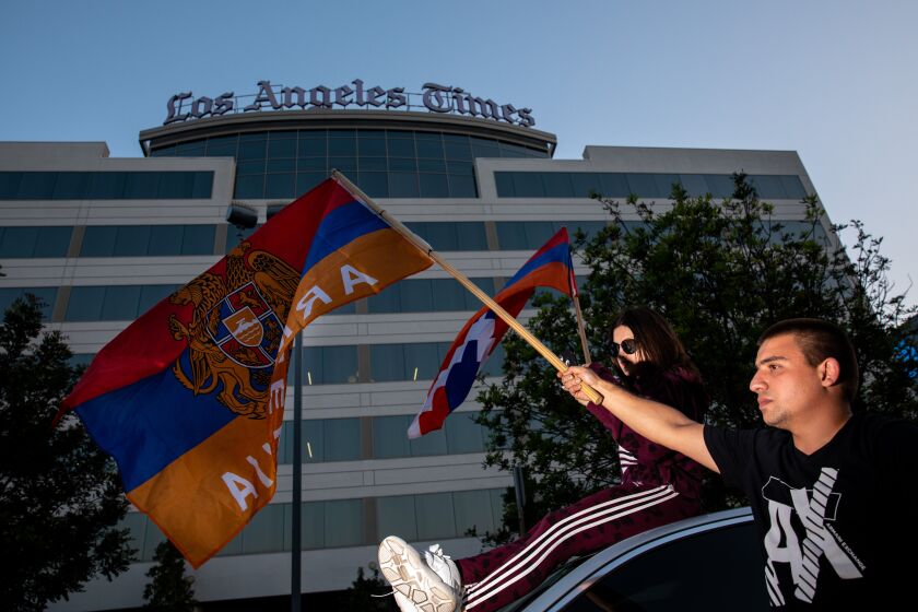 EL SEGUNDO, CA - OCTOBER 06: Suzanna Gevorgyan holds a flag from Artsakh, the disputed region inside Azerbaijan with an Armenian majority population and Haykaz Martirosyan waves an Armenian flag, while More than 1,000 people supporting Armenia with flags, signs and song, gathered in protest of the Los Angeles Times using a quote from the Consul General of Azerbaijan, in a story about the current conflict in the contested Nagorno-Karabakh region between Armenia and Azerbaijan, outside the Los Angeles Times headquarters, in El Segundo, CA,Tuesday, Oct. 6, 2020. Fighting broke out in the region, which Armenians call by its historic name, Artsakh, at the end of September with each side accusing the other of escalation and targeting civilian areas. (Jay L. Clendenin / Los Angeles Times)