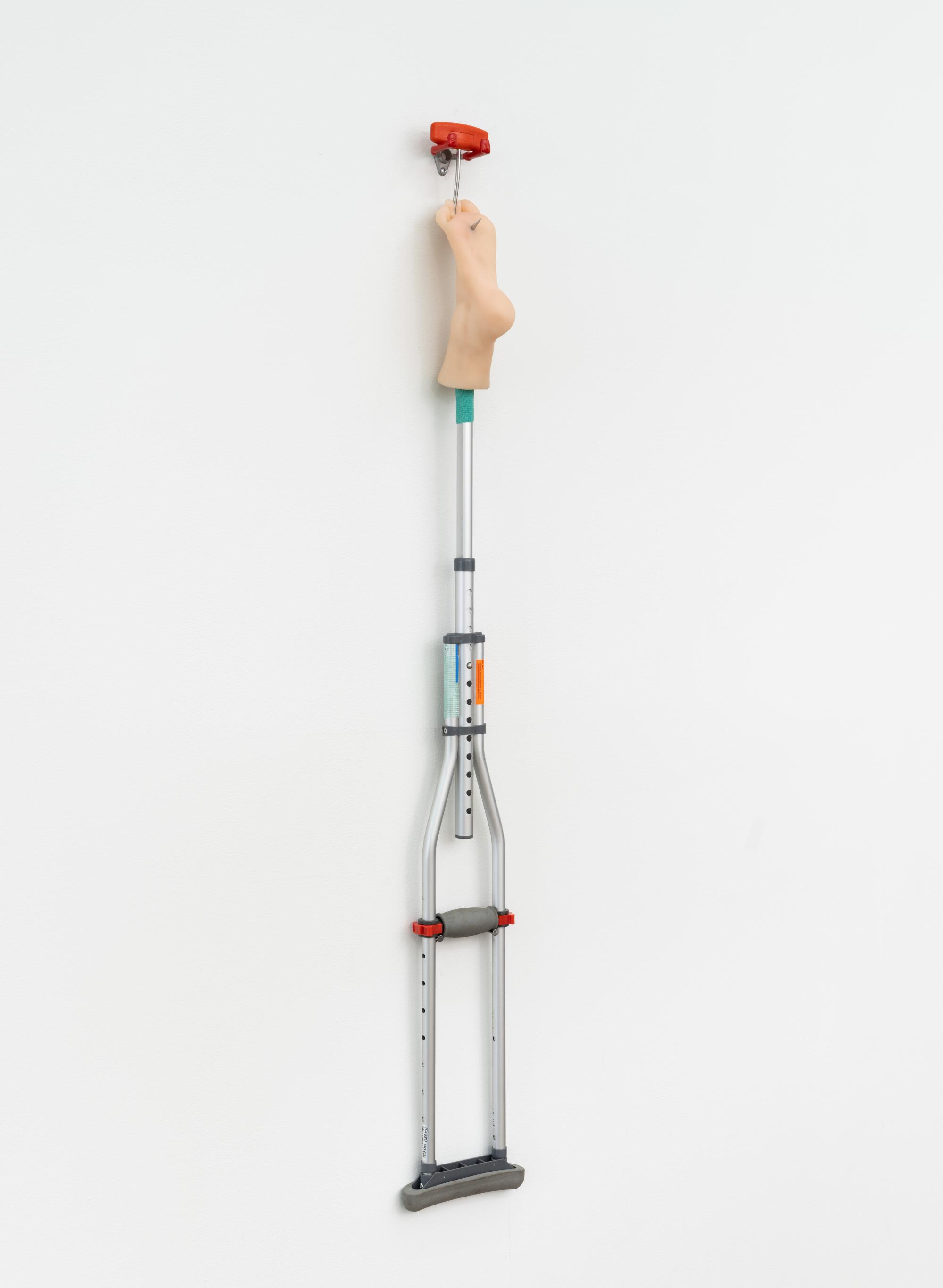 An artwork by Abareshi of a crutch on the wall with a plastic foot at the end.