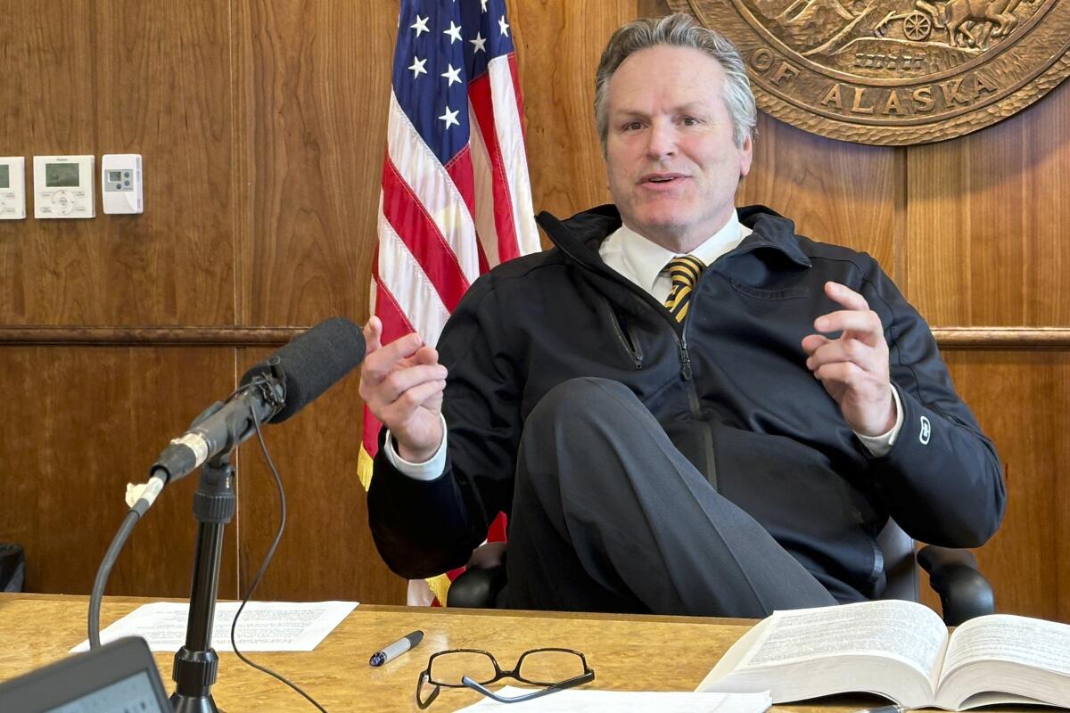 Alaska Gov. Mike Dunleavy gestures while speaking with reporters.