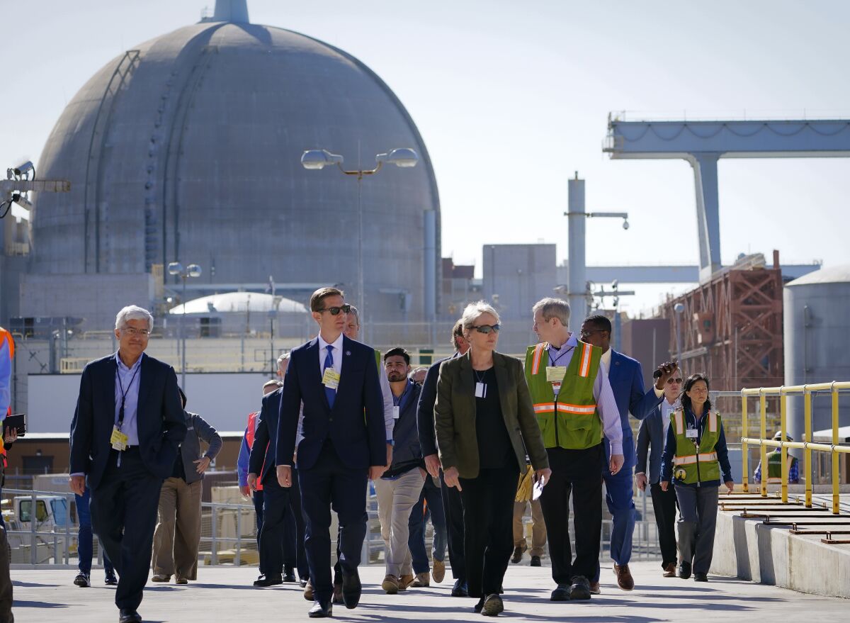 A group of people walks up a wide cement ramp in front of a looming nuclear reactor dome.