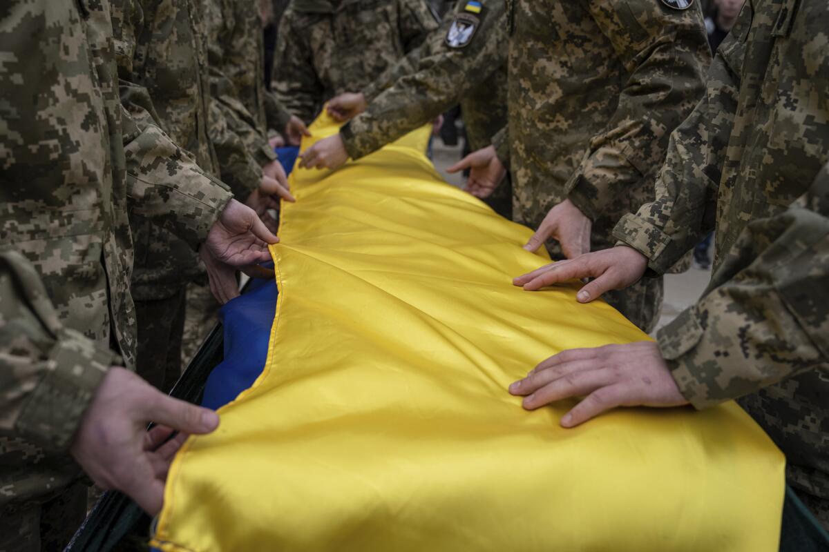 Ukrainian servicemen fold the national flag over a coffin during a funeral ceremony.