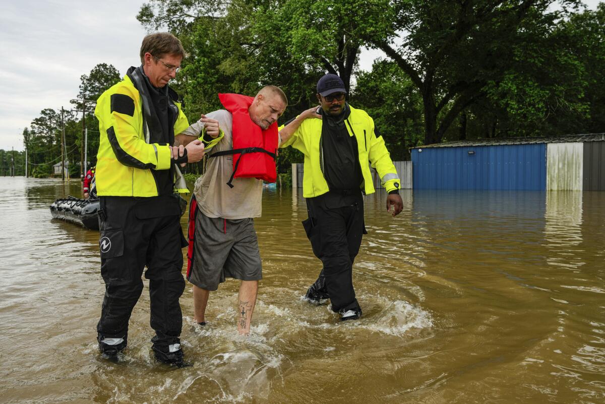 Two rescuers in yellow jackets help a man walk from a boat through floodwaters. 