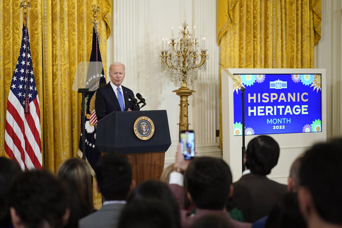 Joe Biden stands at a lectern before a screen bearing geometric patterns and the words "Hispanic Heritage Month 2022"
