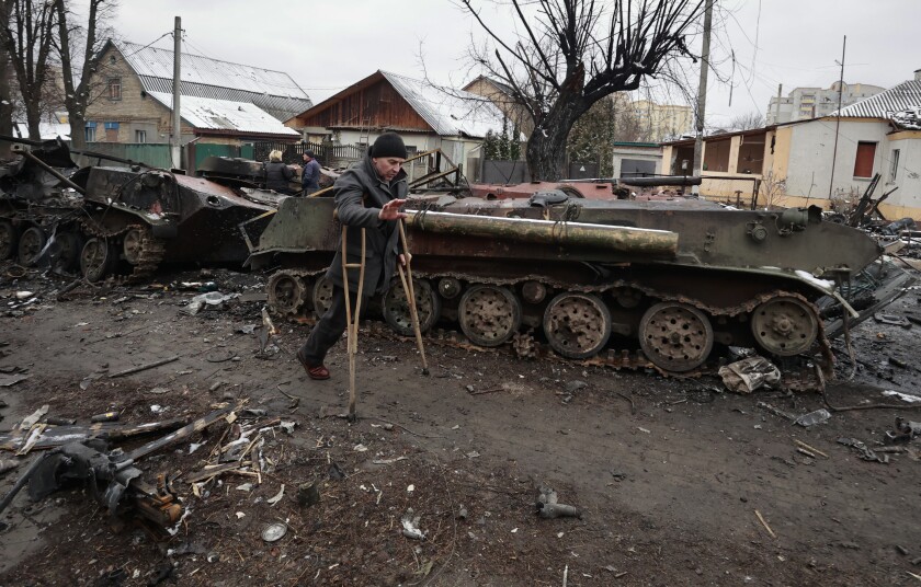 Un hombre con muletas pasa junto a vehículos militares destruidos
