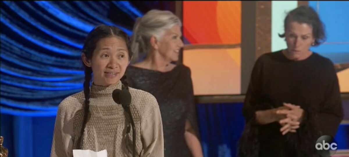 A woman speaks into a microphone while two women stand behind her.