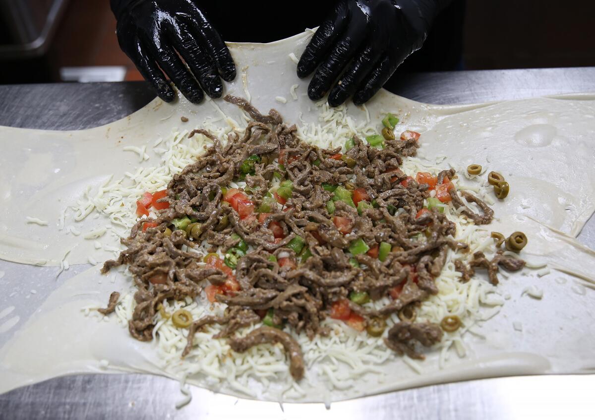 Zarzour folds dough over a beef shawerma pie before setting it in the oven.