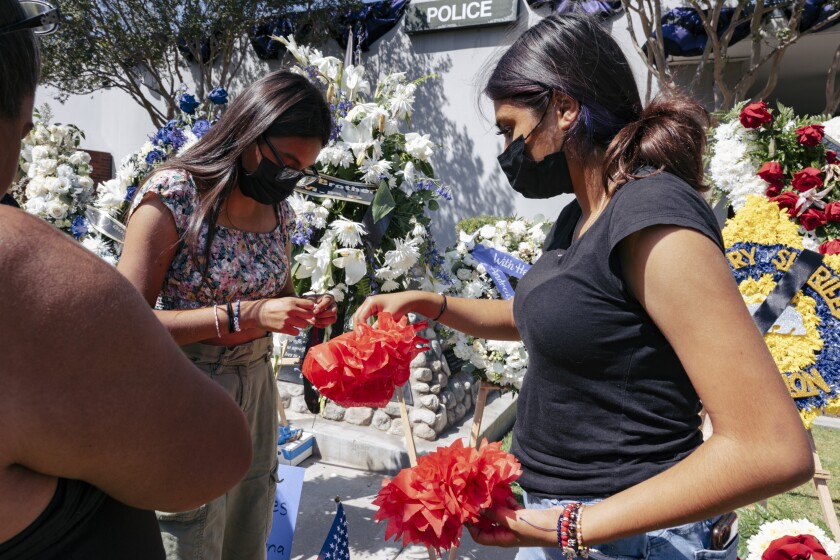 Two high school students tape paper rose to the memorial at the El Monte Police Department.