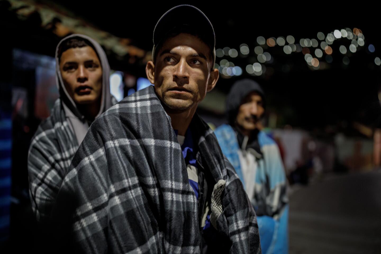Gustavo Rodriguez, center, and friend Jose Toro, left, try to keep warm while waiting to enter a shelter for Venezuelan migrants in Pamplona, Colombia.