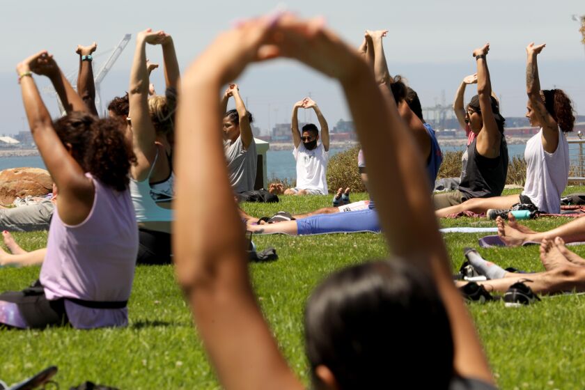 LONG BEACH, CA - JULY 19, 2020 - - People participate in a session of, "Yoga on the Bluff," provided by Yogalution Movement along Ocean Blvd. on Sunday morning in Long Beach on July 19, 2020. According to Dharma Shakti, founder of Yogalution Movement and yoga teacher who leads the class, the Sunday gathering had been shut down for some time due to the coronavirus pandemic. This was the second week that they were allowed to be back in session. (Genaro Molina / Los Angeles Times)