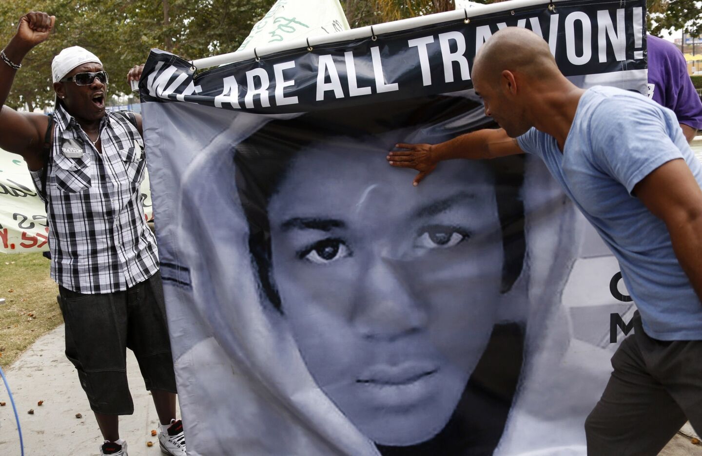 Jeff Sizemore, 51, left, holds a poster of Trayvon Martin as Anthony Walters, 32, pays his respects at a protest rally at Lemeirt Park on July 20.
