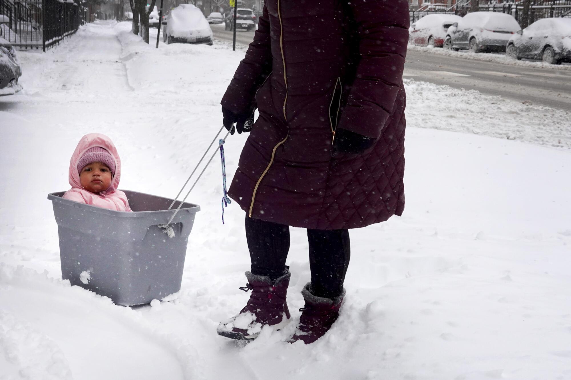 A baby is moved through snow in a plastic container