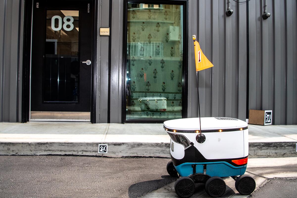 A small robot with six wheels and a yellow flag next to a curbside