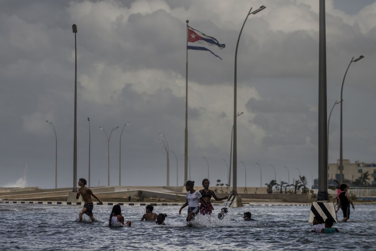 ARCHIVO - Una bandera cubana ondea en lo alto mientras chicos juegan en el mar 