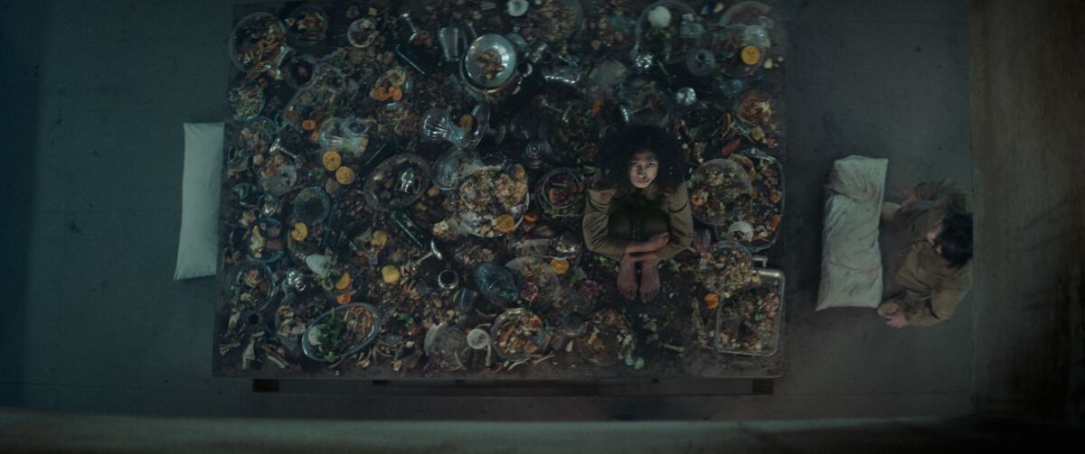 Alexandra Masangkay perches on a spread of leftovers in a scene from Netflix's "The Platform."