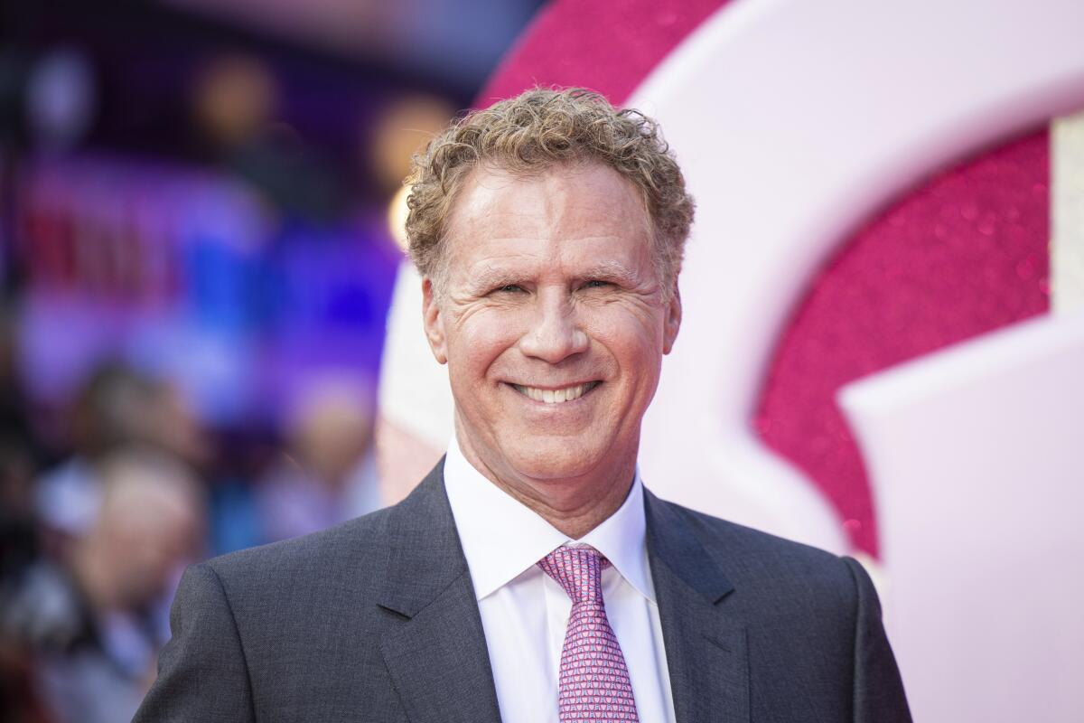 Will Ferrell, in a gray suit and pink tie, smiles at a red carpet premiere for "Barbie."
