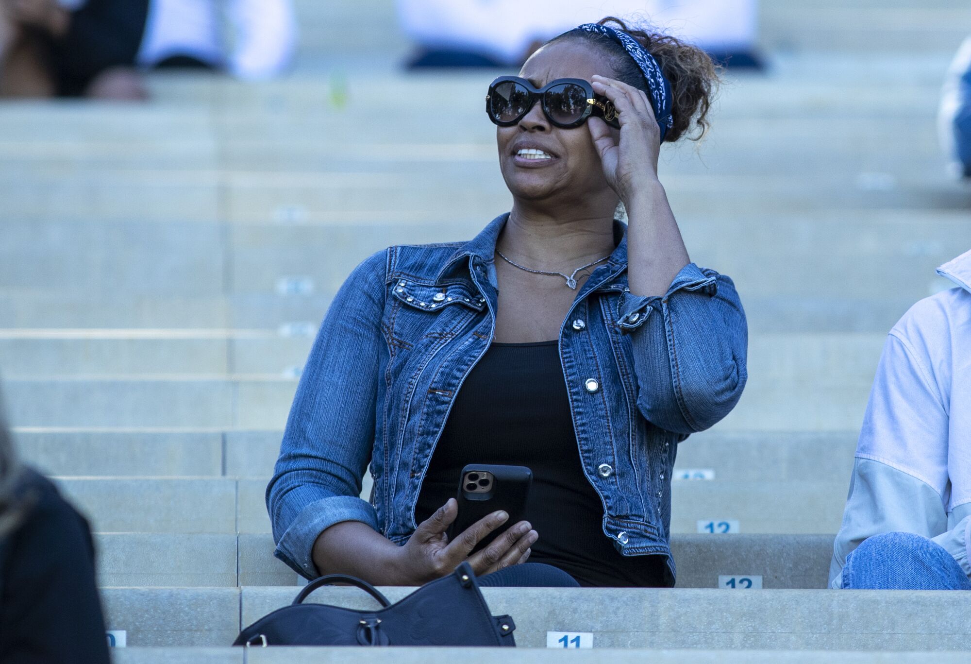 A woman sitting in a grandstand adjusts her sunglasses