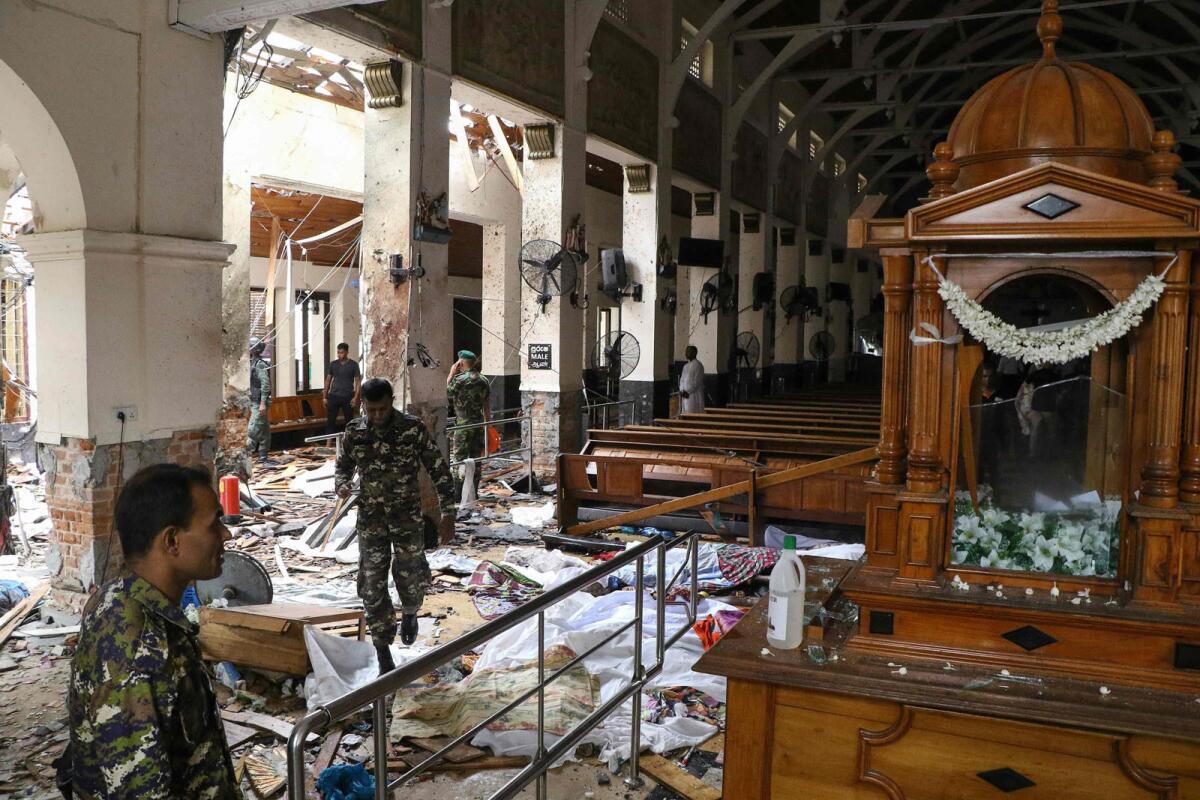 Sri Lankan security personnel pass bodies covered with blankets amid blast debris at St. Anthony's Shrine.