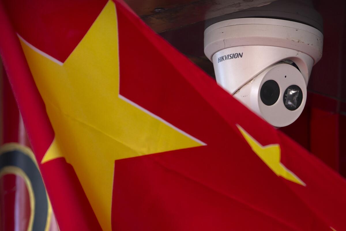 Archivo - Una bandera china cuelga cerca de una cámara de seguridad fuera de una tienda en Beijing 