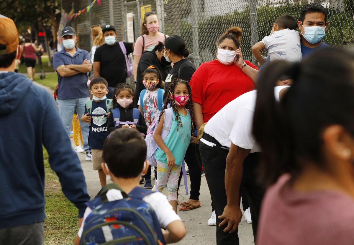 Parents and children wearing masks wait in line outside a school