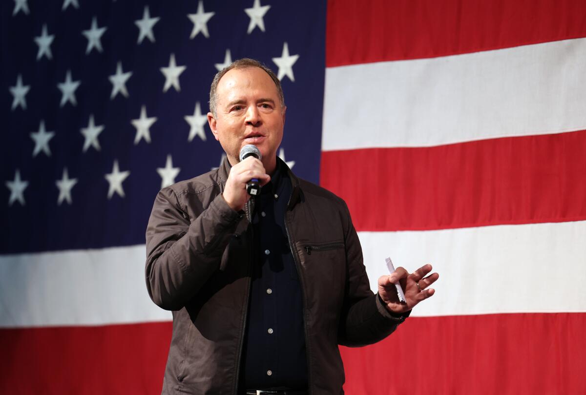 A man holds a microphone in one hand, with an American flag in the background